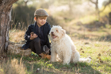 a little boy in vintage clothes walks in nature with a white shaggy dog in spring...