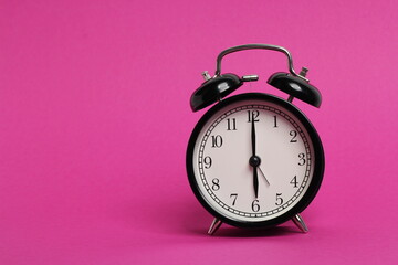 vintage old black alarm clock on pink background