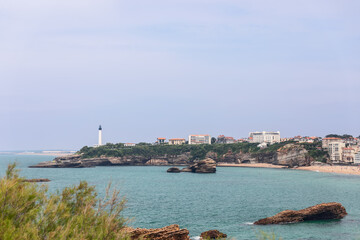 Biarritz city center beachline with Lighthouse under hazy summer sky. Pyrenees-Atlantiques department, French Basque Country