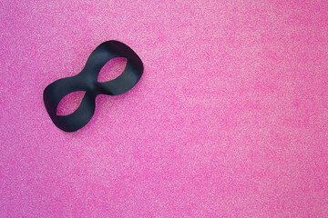 Black carnival mask on a light pink background