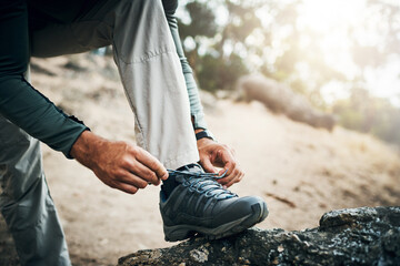 Got to get those shoes tied. Cropped shot of a unrecognizable man tying his shoe laces before going for a hike up a mountain. - obrazy, fototapety, plakaty