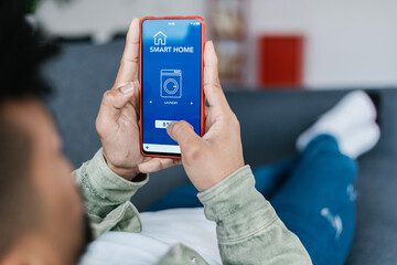 Close up view of young man turning on the washing machine with smart home mobile phone app - IOT or...