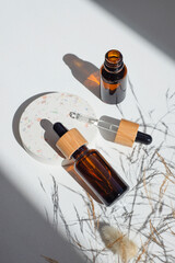 Amber glass dropper bottles with bamboo lid and open pipette with serum or essential oil on white concrete podium for product presentation. Skincare cosmetic. Beauty concept for face body care