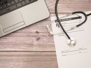 A laptop, a stethoscope on the medical prescription sheet over a wooden table