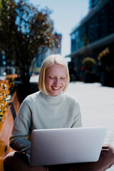 Happy young girl sitting in the park using laptop. Beautiful woman having video call.