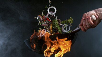 Freeze Motion of Wok Pan with Flying Ingredients in the Air and Fire Flames. - obrazy, fototapety, plakaty