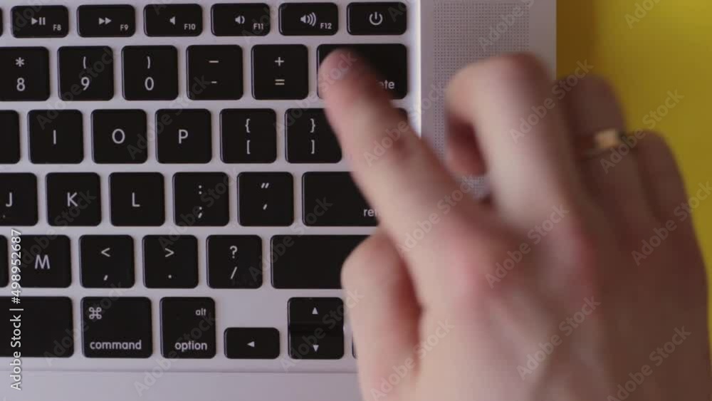 Poster top view of finger frenetically pressing delete button on keyboard, yellow background, static