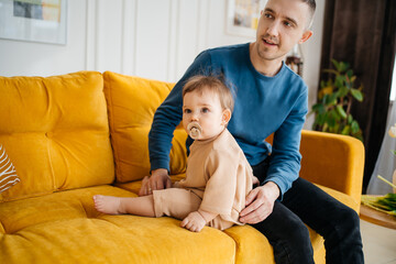 Fototapeta premium child with a pacifier sitting on a yellow sofa with his father