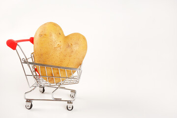 Mini supermarket cart with a large potato tuber in the shape of a heart on a white background.The...