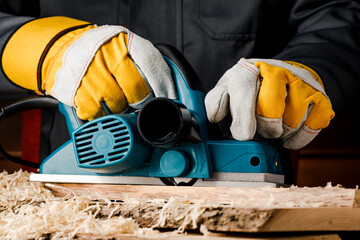 A manual electric plane on a rough log of a tree in the hands of a master. Wood products. Production of wood products.