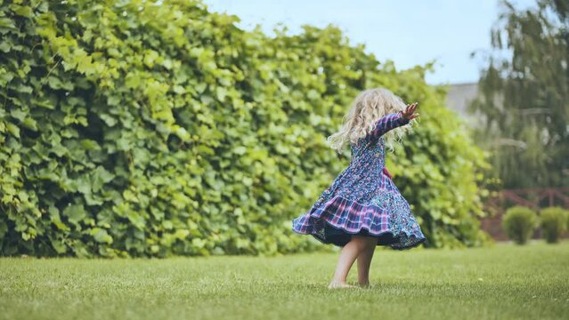A little girl in a dress twirls in the garden.