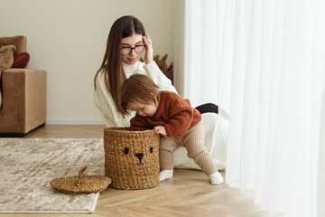 Mom and baby toddler pull toys out of basket. Babysitter and kid playing in room on floor.