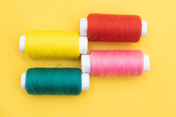 different color yarn or spool thread like rainbow over on yellow background. red,yellow,dark Cyan and pink color yarn