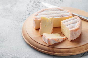 Sliced soft cheese with mold on a wooden board on a gray concrete background