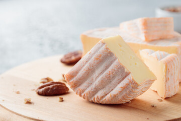 Sliced soft cheese with mold on a wooden board on a gray concrete background