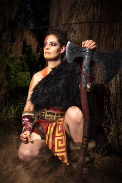 SESION COSPLAY. GUERRERA EN EL BOSQUE, ARMADA CON UN HACHA. FOTOGRAFIA VERTICAL. COLOR.