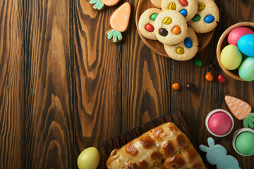 Easter hot cross buns with colored eggs Easter gingerbread rabbits and cookies over dark brown plank wooden old table background. Spring holiday baking concept. Easter table setting. Top view. Mock up