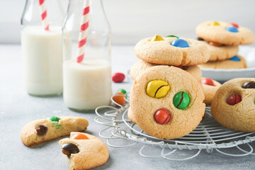 Homemade cookies with colorful chocolate candies and milk. Stack of shortbread cookies with multi colored candy on plate with bottle of milk on light gray background. Baby food concept. Copy space.