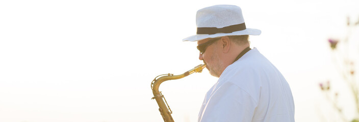 Man playing jazz music on saxophone in the spring nature on a sunny day