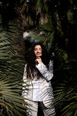 Fototapeta premium dark-haired brunette in a white business-style suit poses in palm trees. vertical photo