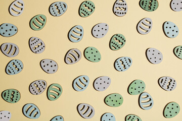 Pastel green, purple and blue wooden eggs arranged on pastel beige background. Minimalist spring and Easter layout.