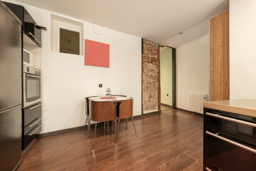 Kitchen with dining table with brown wooden design chairs, column of appliances and gray furniture and wooden floors