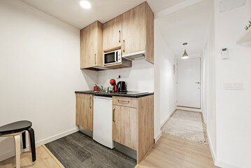 Kitchen with dark gray countertops, wood cabinets, and built-in white appliances next to a foyer...