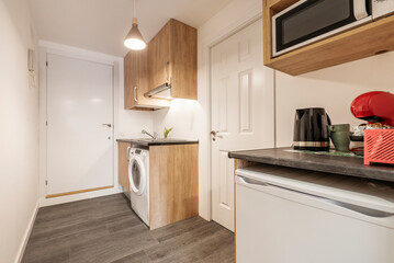 Kitchen with dark gray countertops with small appliances above it, wood cabinets, and built-in white appliances next to a foyer in a vacation rental apartment