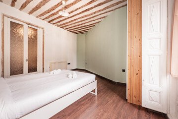 Bedroom with a large bed with white linens, exposed wooden beams on the ceiling and a balcony with white wooden shutters