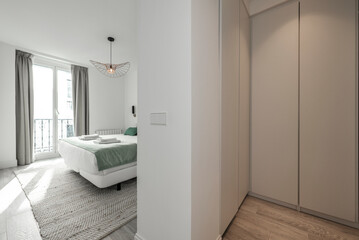 Fototapeta na wymiar Bedroom with a large bed with white sheets, clean white towels, a white wooden balcony, a brown parquet floor and cabinets with gray wooden doors in the dressing room