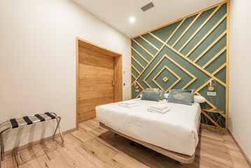 Bedroom with large bed with white sheets, clean white towels, wall decorated with wood and pale green paint, chestnut wood floors, large wooden sliding gate in vacation rental apartment