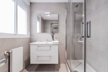 Bathroom with aluminum window, frameless wall mirror, white porcelain sink on white marble top and shower cabin with glass screen and water jets