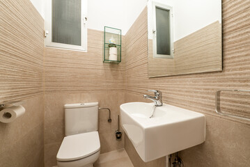 Fototapeta na wymiar Small cloakroom with white porcelain sink, frameless mirror, and cream tile