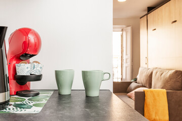 Corner of a kitchen with a red pod coffee machine next to pale green mugs next to a vacation rental...