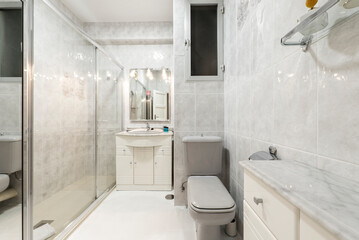 Bathroom with imitation marble tiling and frameless wall mirror, white porcelain sink above vanity and white marble countertop with gray veining