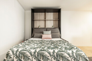 Extended pull-out bed with cushions, plant-print blankets and white bedding in a short-term rental studio