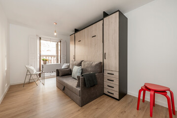 Extended pull-out bed with cushions, blankets and white bedding in short-term rental studio apartment with white vintage wooden balcony
