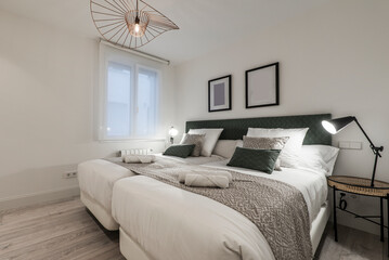 Twin beds attached with headboard upholstered in green fabric with matching cushions and twin bedside tables with lamps