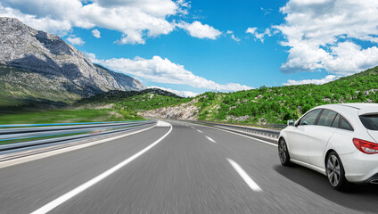 Fototapeta premium White car on a scenic road. Car on the road surrounded by a magnificent natural landscape.