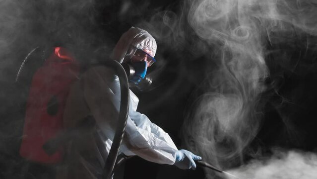 Disinfection Work Aarea. A man in a protective suit, glasses and a respirator sprays a disinfectant. At the same time, he makes a gesture meaning Ok!