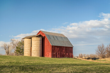 old red barn with twin silo and irrigation ditch at Colorado foothills, early spring scenery at...