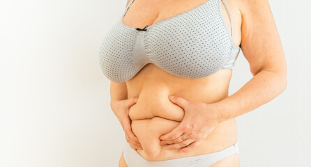 overweight woman holds fold of excess fat on stomach