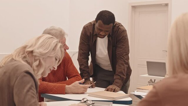 Medium slowmo of African American personal growth coach helping group of seniors doing tests during self development training