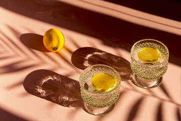 Two glasses of water with sliced lemon on sunlit background with shade. Summer refreshment concept....