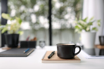 Black coffee cup and black pen and notebook on white table