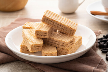 Wafer with coffee flavored cream in white plate with cup and coffee bean background