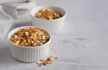 A white bowl of homemade muesli on a light table. Granola with nuts and dried fruits for a healthy breakfast. Copy space. Selective focus.