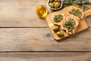 Tasty bruschettas with pesto and rosemary on wooden table, flat lay. Space for text