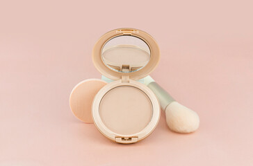 Beige face powder on a pink background. Studio photography. Open powder with sponge and brush on the background.