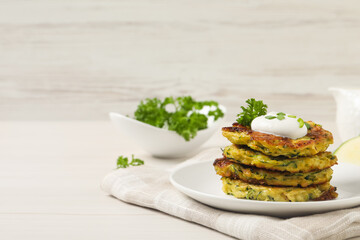 Delicious zucchini fritters with sour cream served on white wooden table, space for text